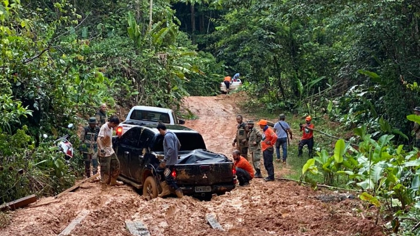 A pick-up truck stuck in the mud with crews standing around in the rain forest 
