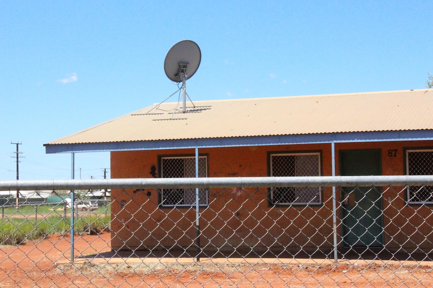 An orange house in an arid street scape is behind a fence