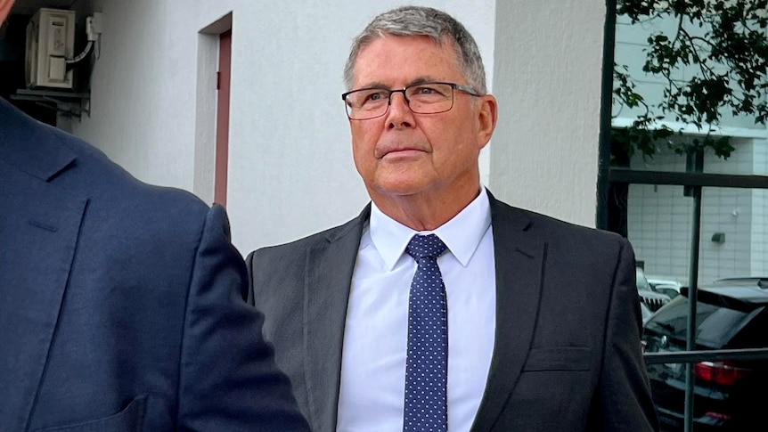 A grey-haired, bespectacled man in a suit outside a court building.