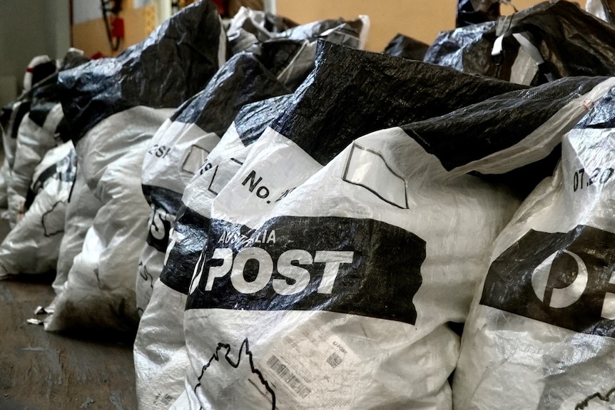 Fileiras de sacolas pretas e brancas com 'Australia Post' escrito nelas.