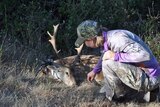 A woman in purple and grey clothing with a gun and a dead deer.