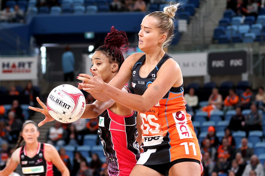 A Giants Super Netball player competes for the ball alongside an Adelaide Thunderbirds opponent.