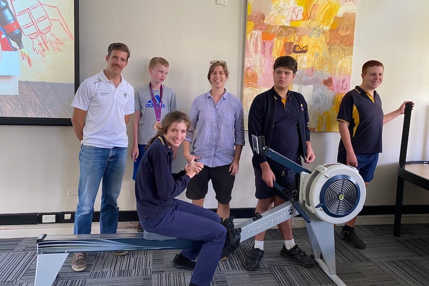 Chris Morgan stands with school children around a rowing machine.