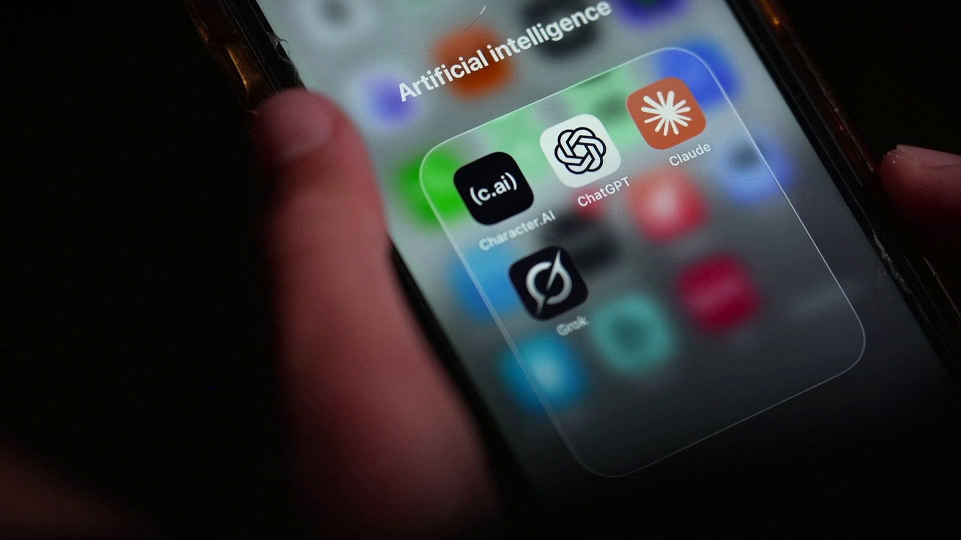 A person holding an iPhone with Character.aI, ChatGPT, Claude and Grok chatbot apps on screen.