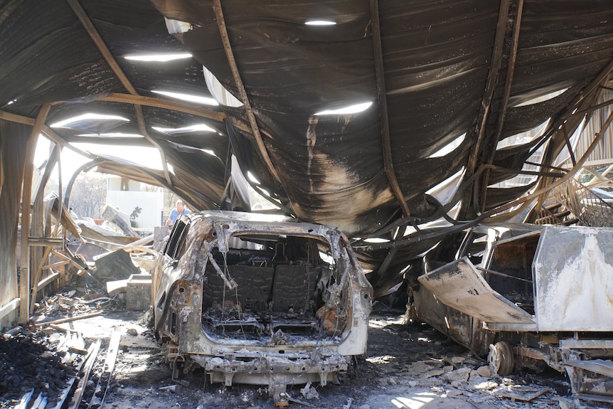 A burnt out car inside a collapsed shed.