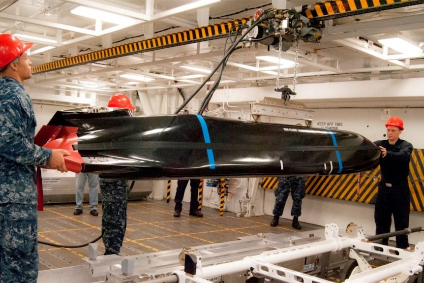 Crew members work on a large missile in a hangar.