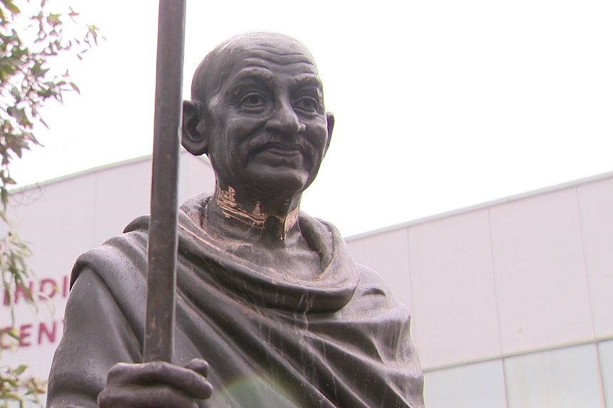 A close-up of a statue of Mahatma Gandhi with damage around its neck.