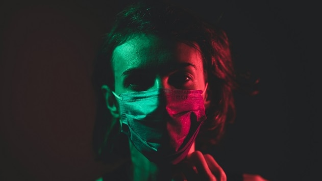 A woman wearing a surgical mask is lit up by red and green lights