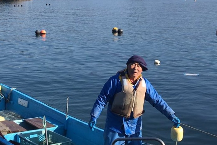 Japanese fisherman on his boat with islands in the distance in Rikuzentakata prefecture