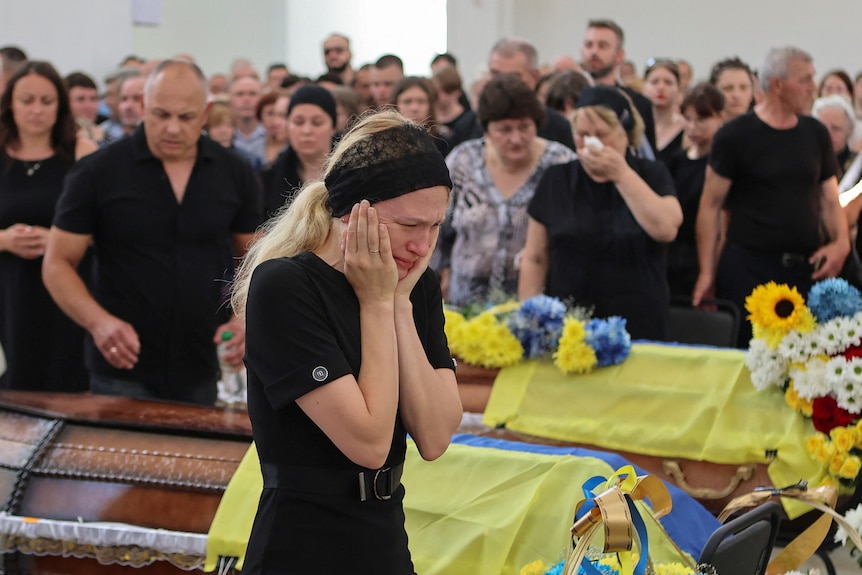 Woman in black crying next to coffins draped in the Ukrainian flag