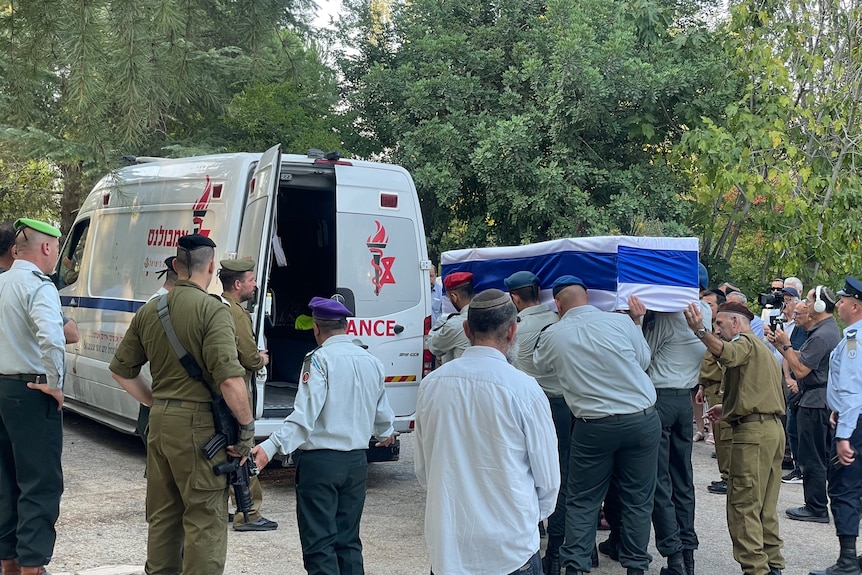 Israeli soldiers retrieve a coffin, draped in an Israeli flag, from a parked ambulance