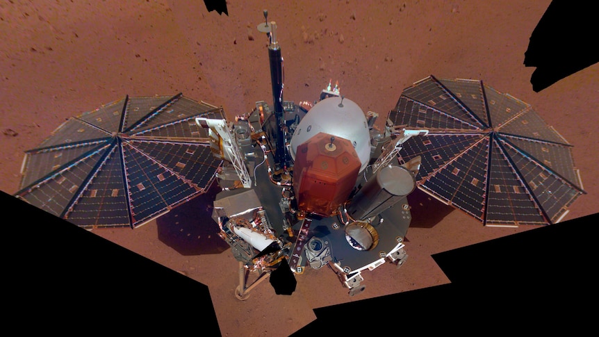 A machine with two solar-panel fans either side of a central box sits on a red surface