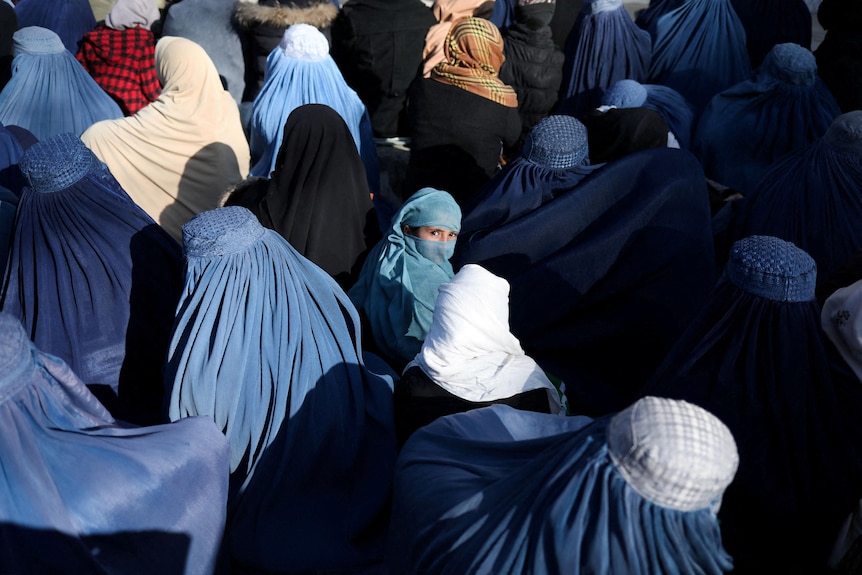 A girl sits among a crowd of people all wearing blue and white hijabs.