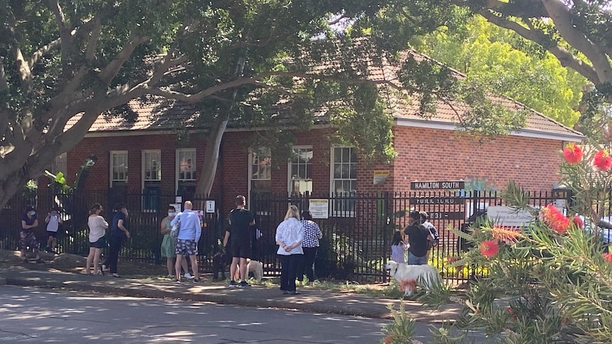 A group of parents lined up out the front of a primary school wearing masks