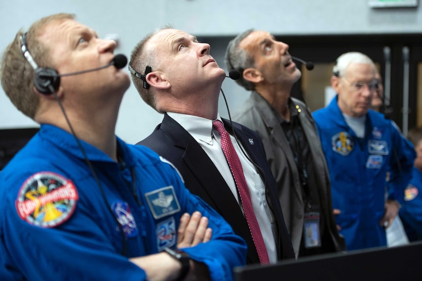 Four NASA officials looking up while wearing headsets