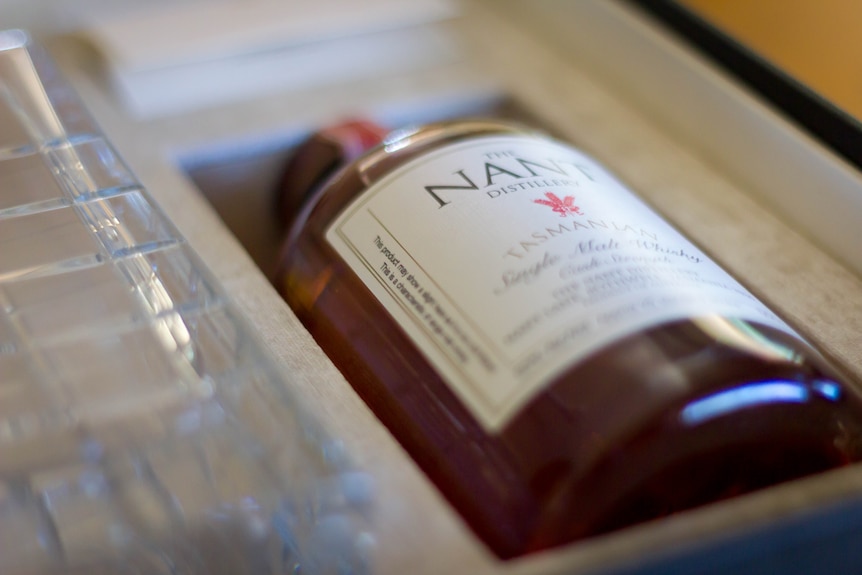 A whisky bottle sits in a wooden case.