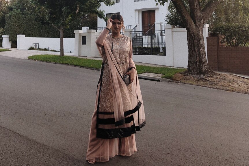 A photo of Zathia wearing traditional cultural clothing as she stands in a neighbourhood street. 
