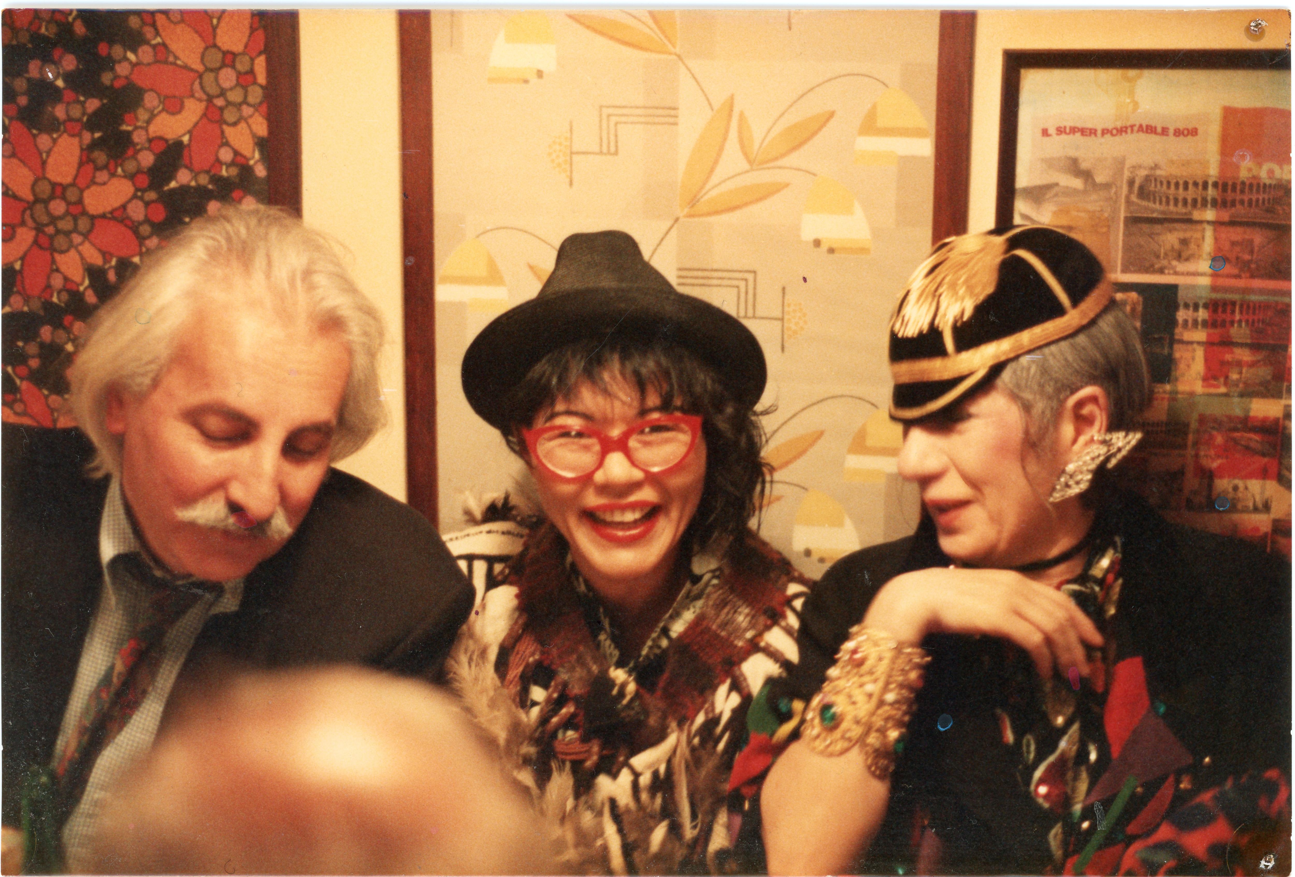 Two women wearing flamboyant clothes sitting at a restaurant table.