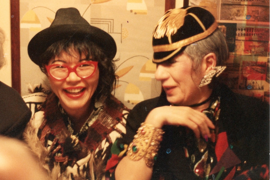 Two women wearing flamboyant clothes sitting at a restaurant table.
