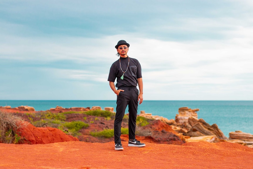 Man standing in stylish outfit, on front of red rocks and ocean