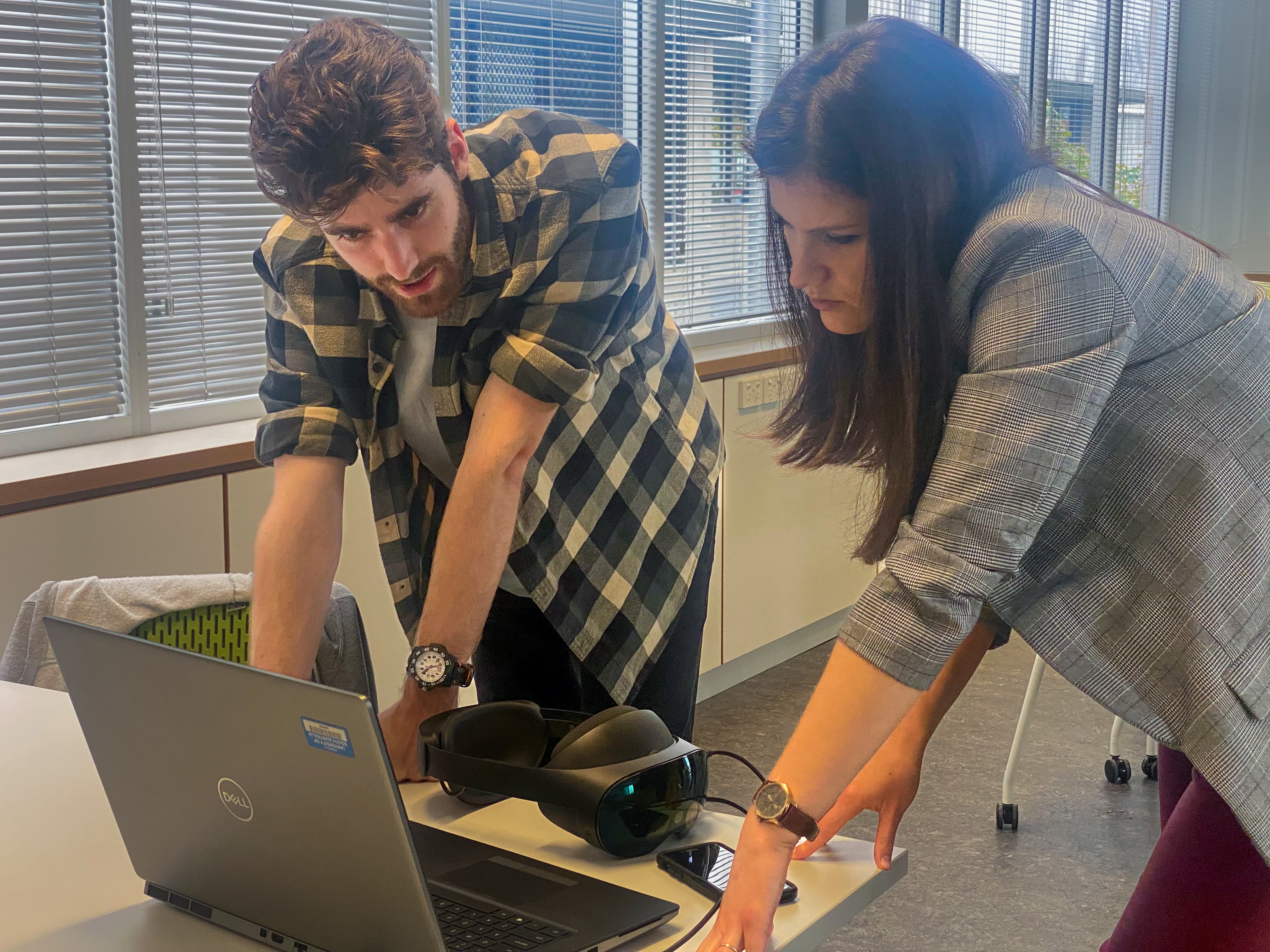A man and women crouch over a laptop at a desk reviewing its results. 
