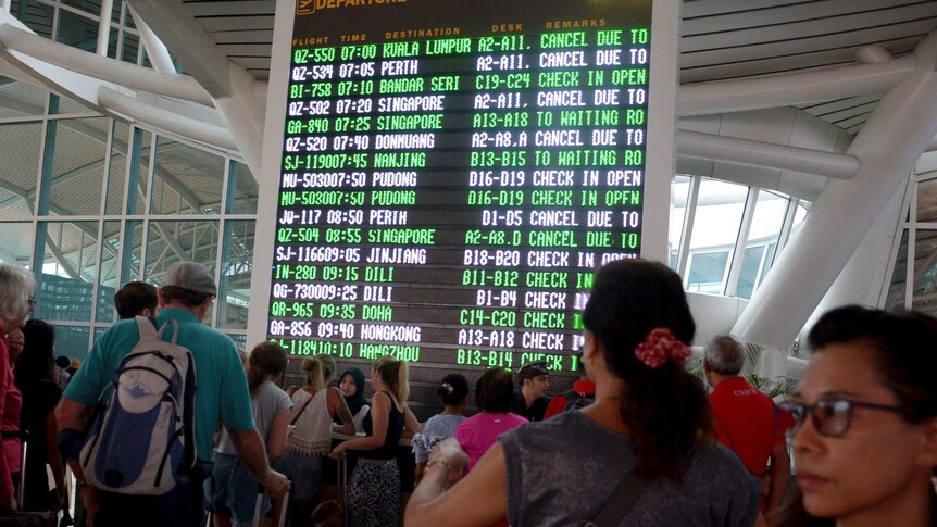 A flight information board shows cancelled flights at Bali's main airport, as passengers crowd around it with their luggage.