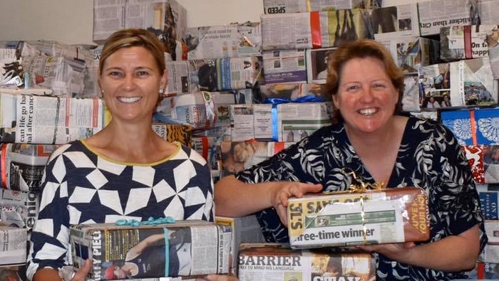 Two women standing in front of newspaper covered boxes, they are both holding boxes
