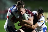An NRL player tries to drive forward as he is grabbed by two defenders.