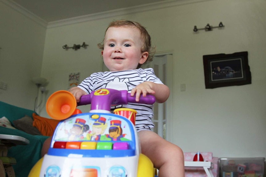 Toddler Aviana McElwee at play on a bike with wheels in her lounge room.