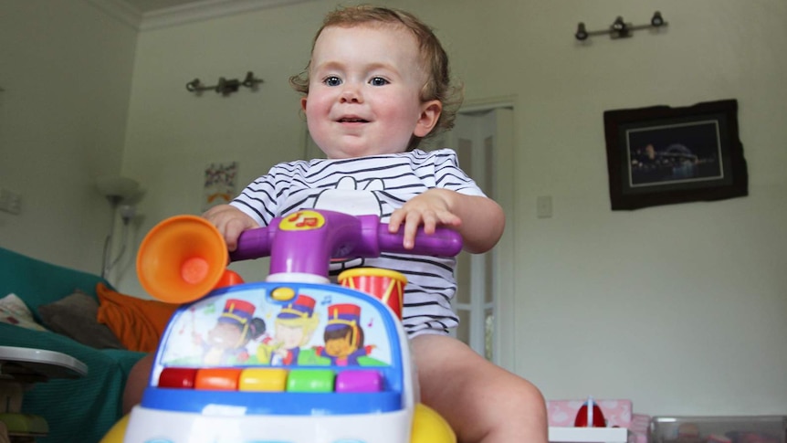 Toddler Aviana McElwee at play on a bike with wheels in her lounge room.