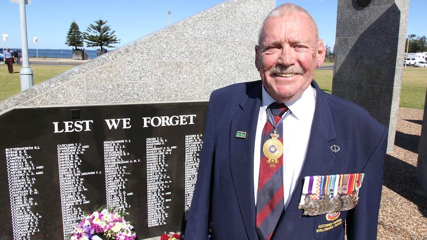 A man stands in front of a war memorial emblazoned with 'lest we forget'