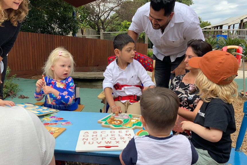 Kayaan Katyal at a table covered with puzzles, with his parents and three other young children.