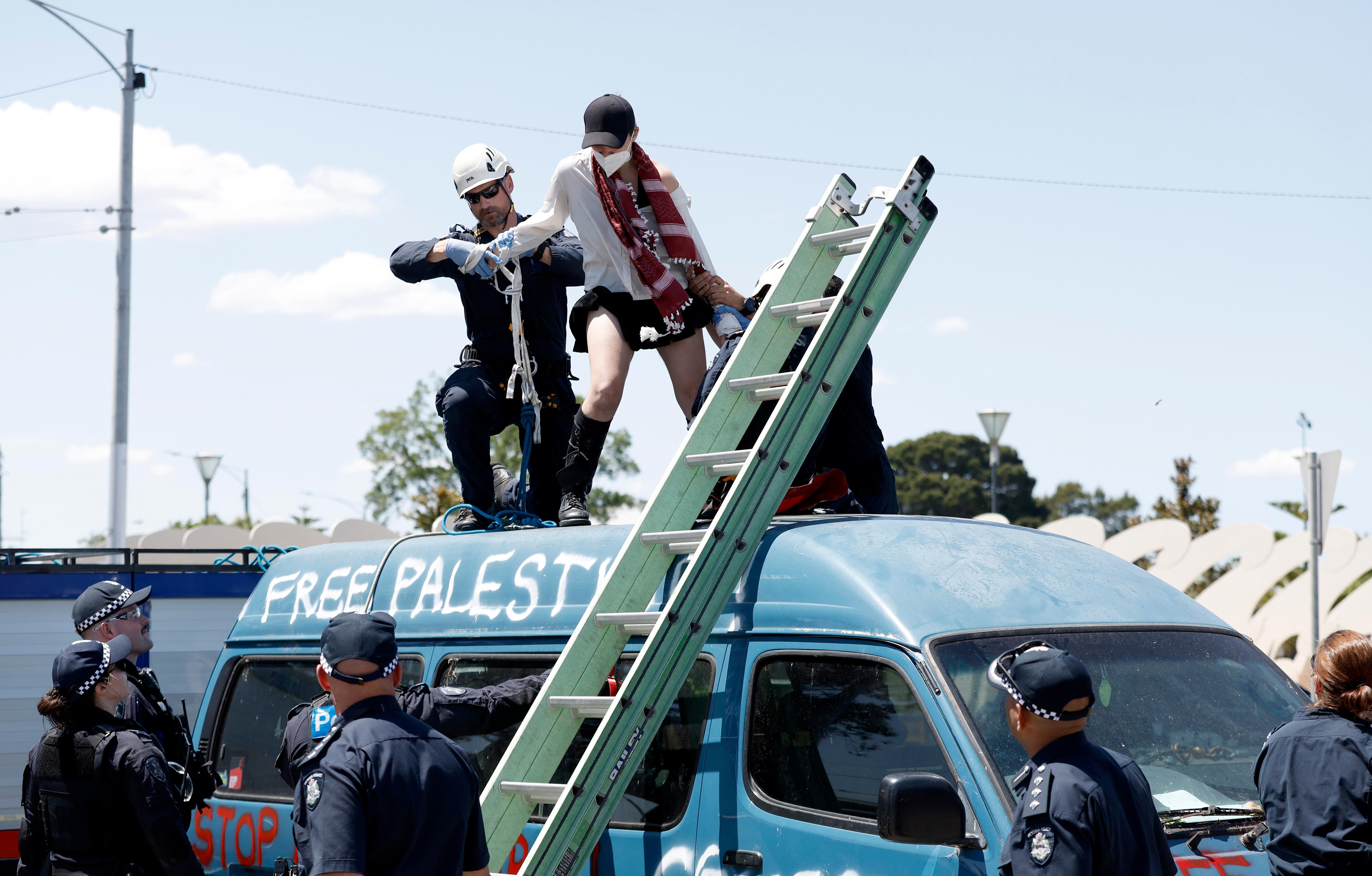 A woman on top of a blue van is arrested by a police officer.