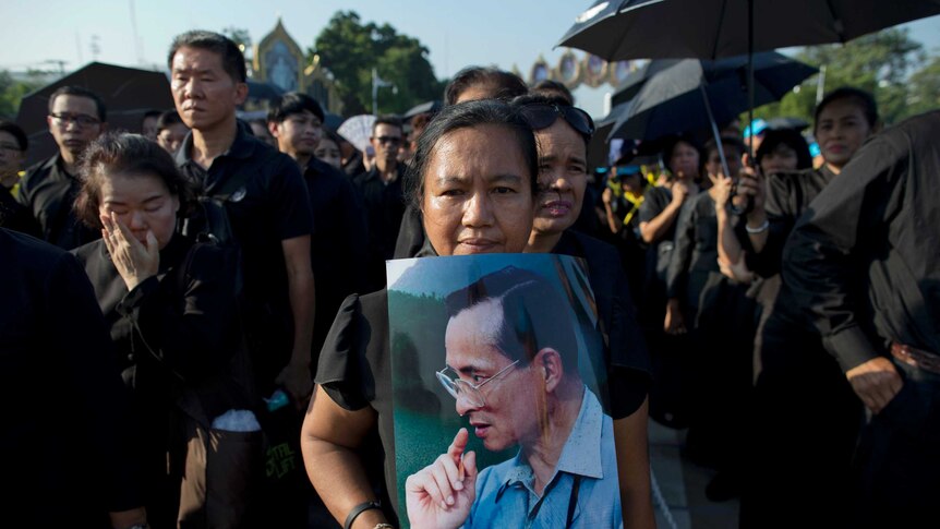 Thai mourners stand in a line to pay respect to a portrait of late Thai King Bhumibol Adulyadej. They are all dressed in black.