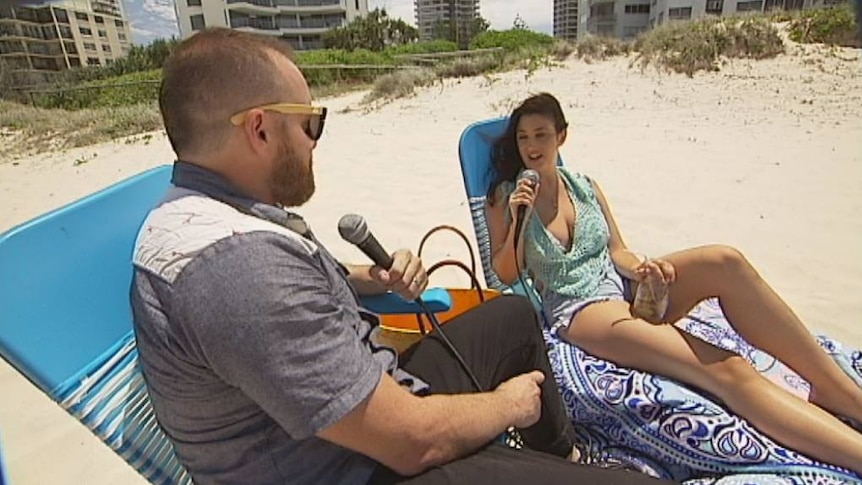 Man sits on a beach chair and interviews a woman on a Gold Coast beach