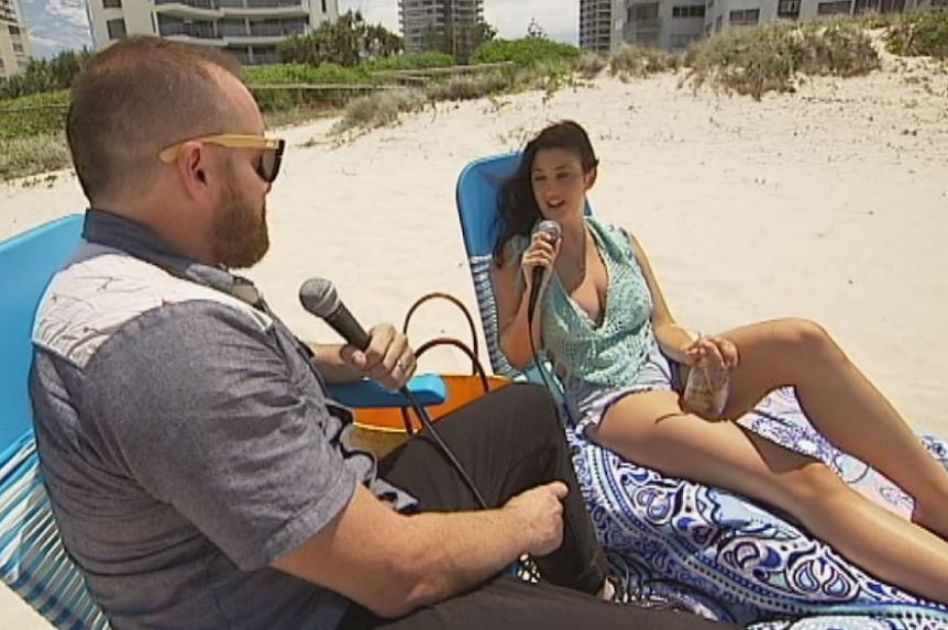 Man sits on a beach chair and interviews a woman on a Gold Coast beach