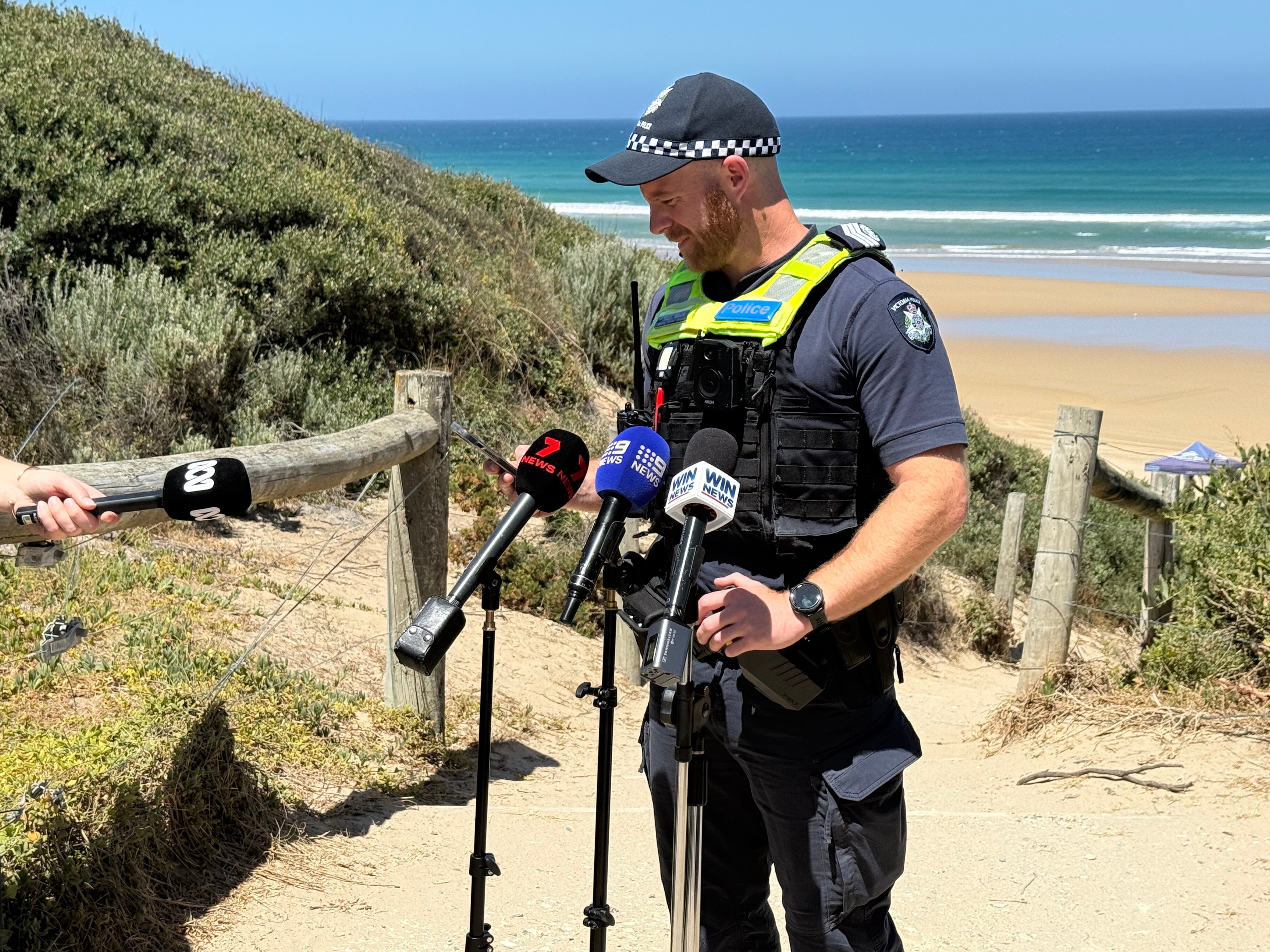 Una foto de un oficial de policía con un chaleco verde fluorescente brillante y parado en la playa con una gorra azul oscuro.