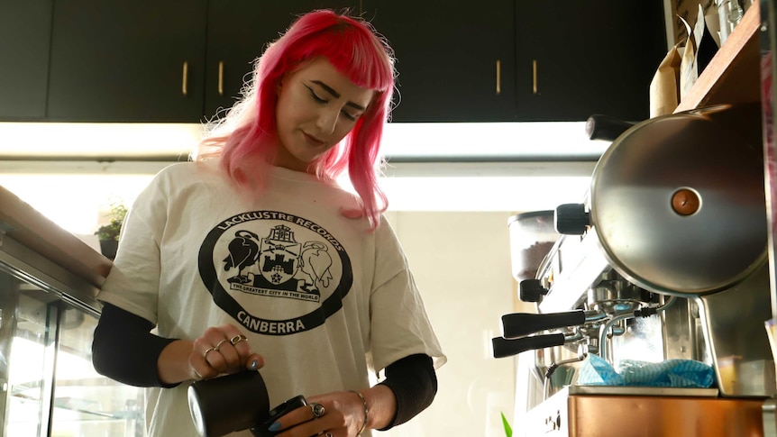 A woman with bright pink hair makes a coffee.