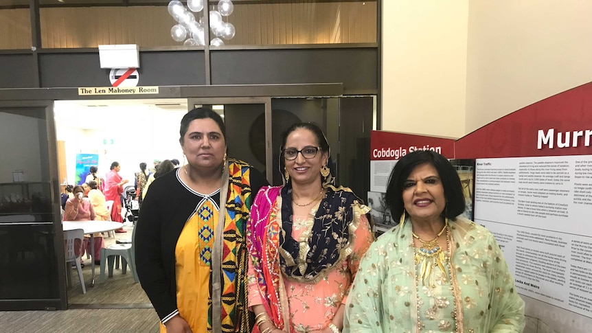 Manjit Bhullar, Balwinder Kaur and Molly Johal in traditional Indian dress at a town hall.