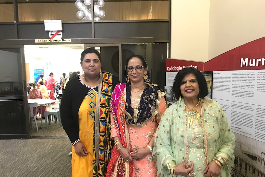 Manjit Bhullar, Balwinder Kaur and Molly Johal in traditional Indian dress at a town hall.