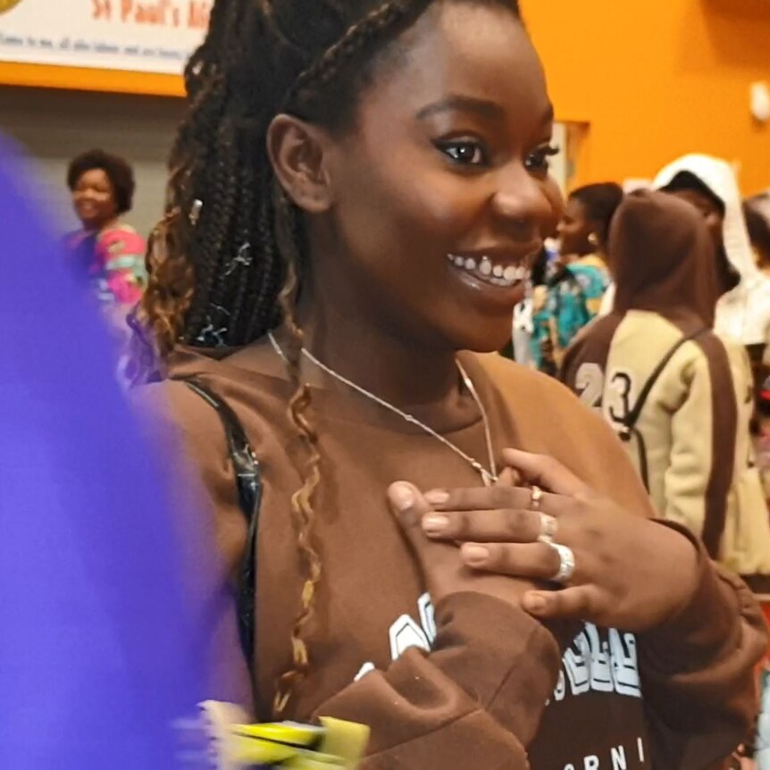 An African girl with a big smile holds her hands to her chest in joy