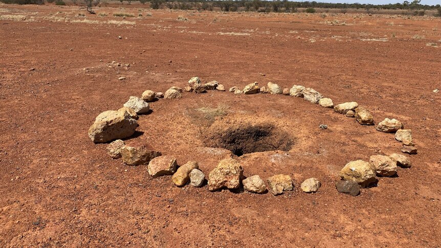 A circle of rocks surrounding a hole in the ground in an outback paddock.