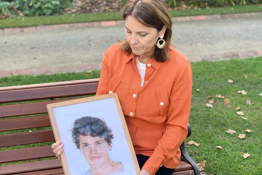 Loretta Gabriel sits on a park bench, holding a photo of her son Sam.