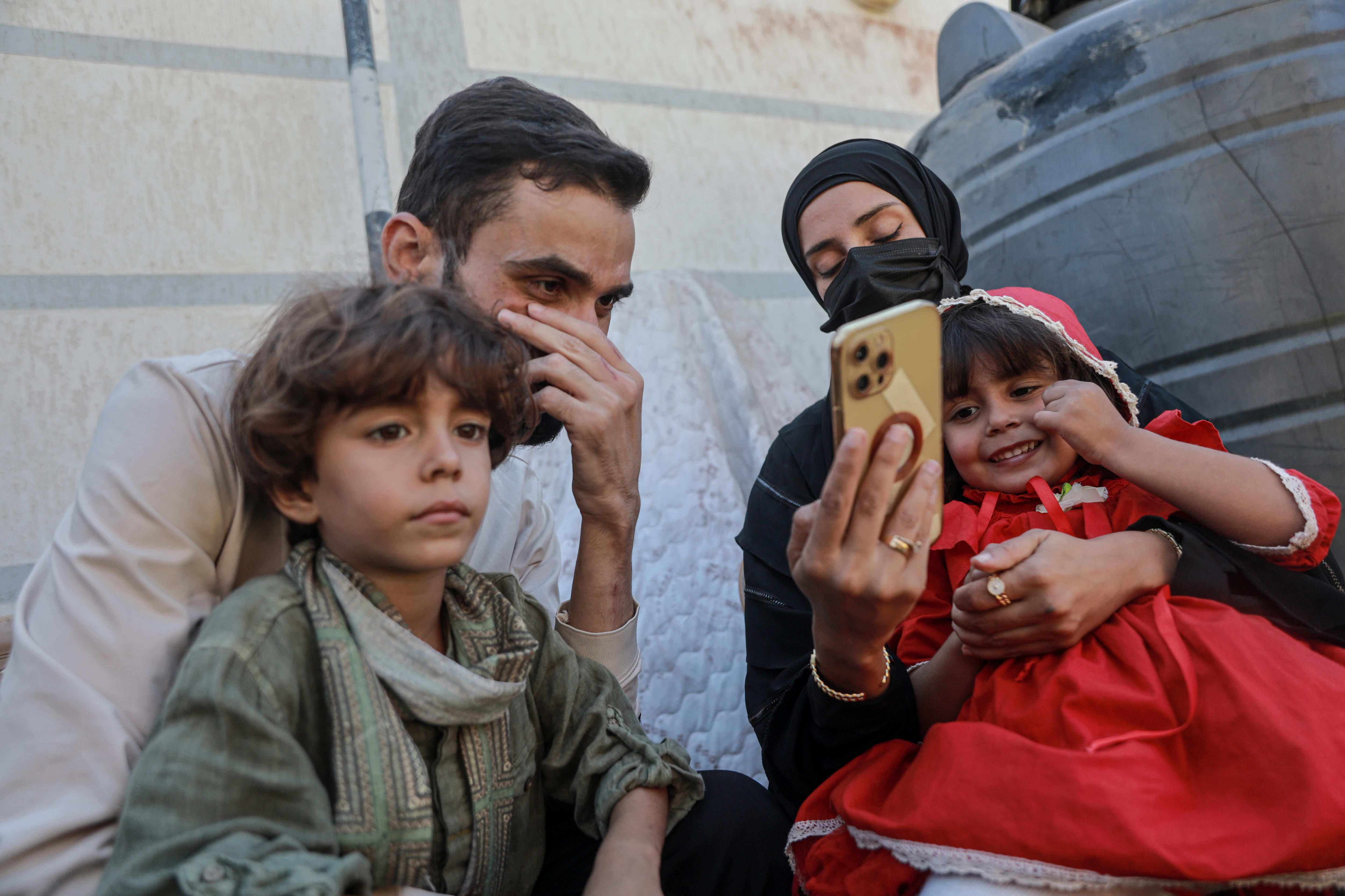 Shadi Abu Sido wipes his eyes, surrounded by his two children, as his wife shows him photos on her phone