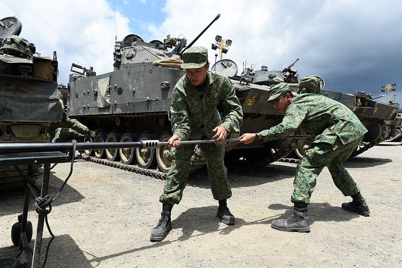 2 soldiers pulling metal rod in front of tanks