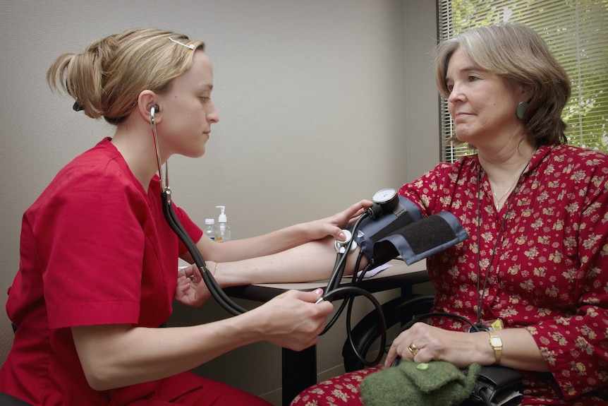 Two women sit opposite each other - one is a doctor testing an older woman's blood pressure.
