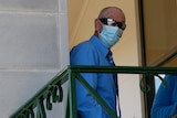 man with sunglasses and a facemask and a blue shirt standing outside courthouse