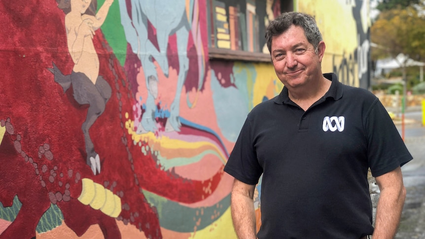 Peter Barr, standing with his hands in his pockets, in front of a brightly painted street mural.