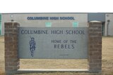 The exterior of Columbine High School is seen, with an engraving that reads, 'Home of Rebels'.