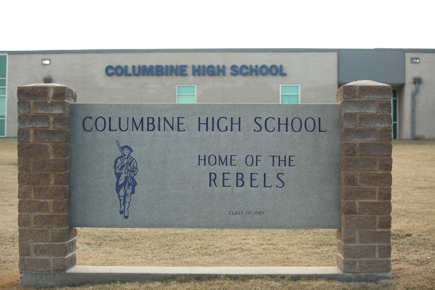 The exterior of Columbine High School is seen, with an engraving that reads, 'Home of Rebels'.